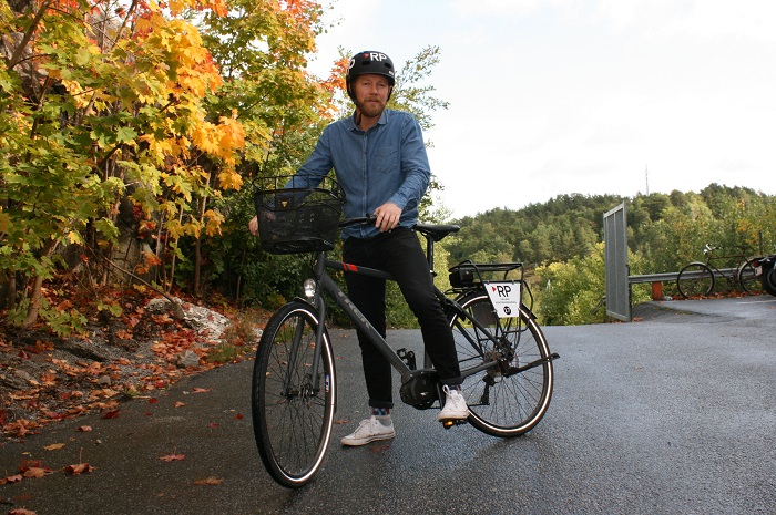 Man med hjälm och cykel framför träd med gula löv.