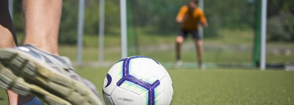 Närbild på en fot, fotboll och målvakt.