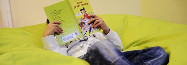 Ett barn som ligger och läser en bok i en gul saccosäck