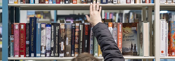 En bibliotekshylla och en hand som sträcker sig efter en bok