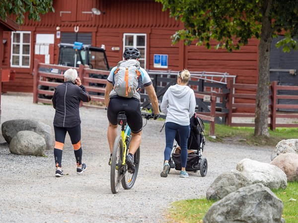 En cyklist, en löpare och en vuxen med barnvagn intill bondgården