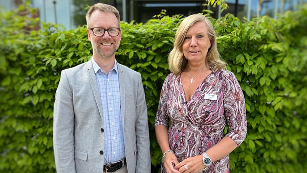 En man och en kvinna leendes in i kameran framför en grön häck.